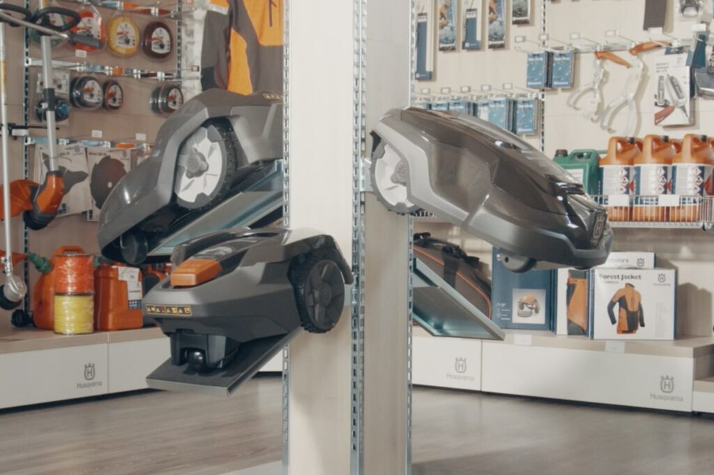 AWService-Laden mit einer Auswahl an Werkzeugen und Equipment. Im Vordergrund eine Säule mit Halterungen, die diverse Mähroboter präsentiert