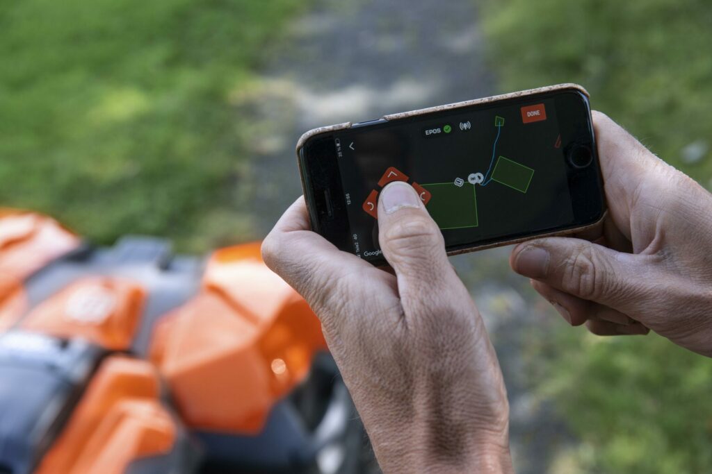 Eine Person steuert einen Mähroboter über ihren Smartphone